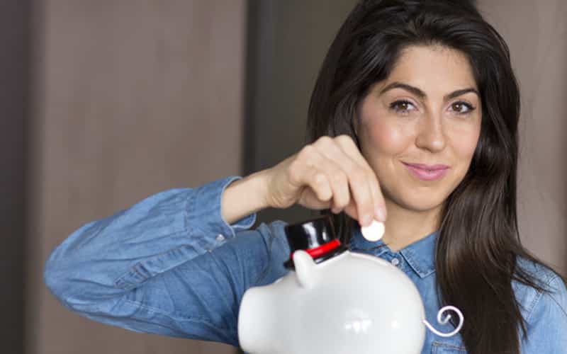 Young Woman Putting Coin into Piggy Bank